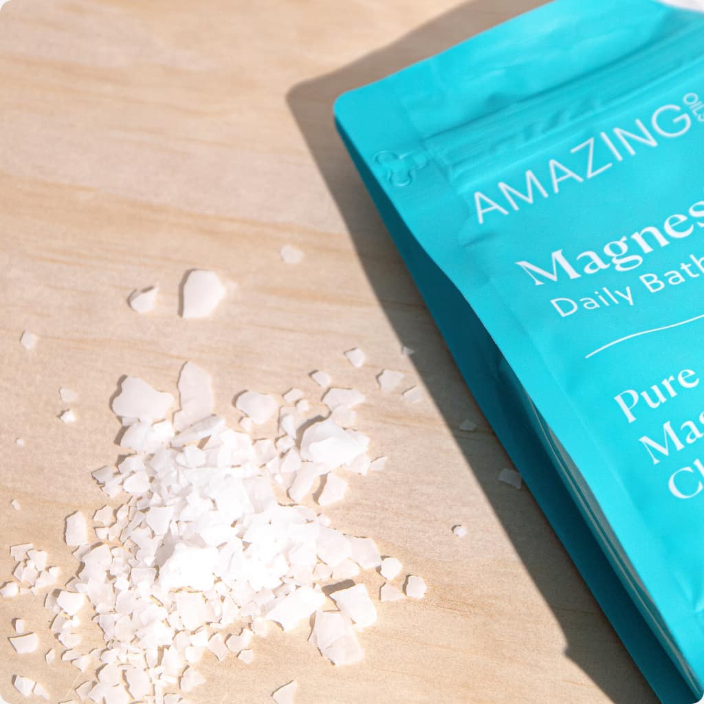 Blue packaging of 'AMAZING' bath salts on a wooden surface with some of the salt crystals spilling out. Pure magnesium flakes for bath or foot soaks—ideal for soothing muscles, stress balance, and natural detox without additives. Amazing Oils Australian stockist. Geelong based. Shop now!