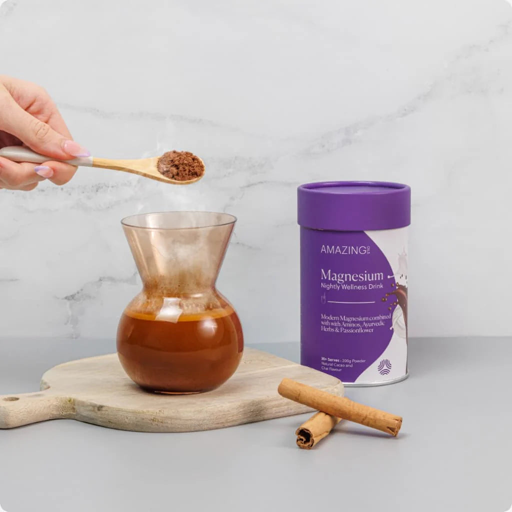 Person adding powder to a glass of liquid next to a container labeled 'Amazing!' on a marble surface. Cacao‑chai bedtime drink with magnesium, ashwagandha, and calming botanicals for stress relief and natural sleep support. Amazing Oils Australian stockist. Geelong based. Shop now!