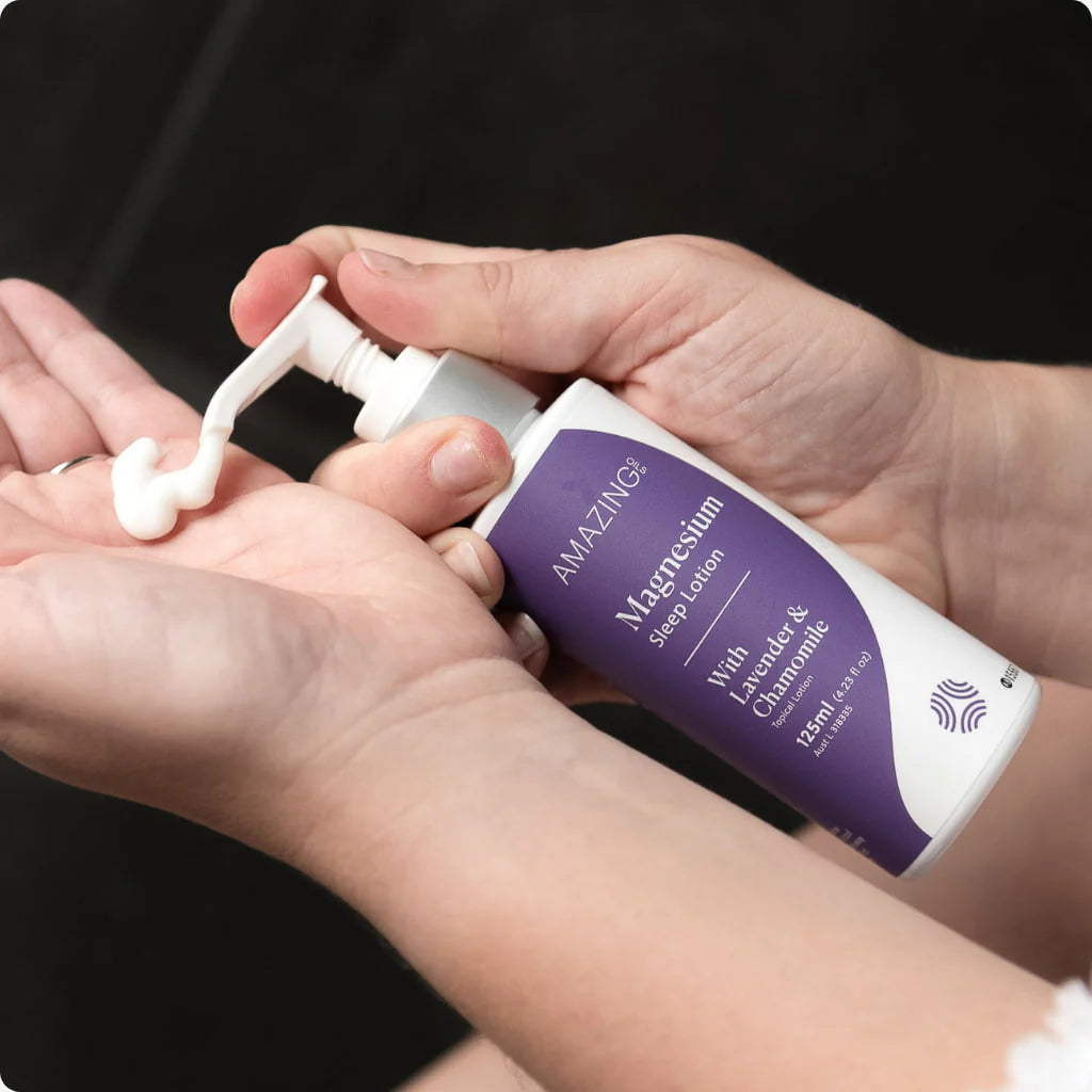 Person holding a bottle of magnesium lotion with a dark background. Bedtime magnesium lotion with lavender and chamomile to support deep sleep, reduce stress, and calm the body—no melatonin needed. Amazing Oils Australian stockist. Geelong based. Shop now!